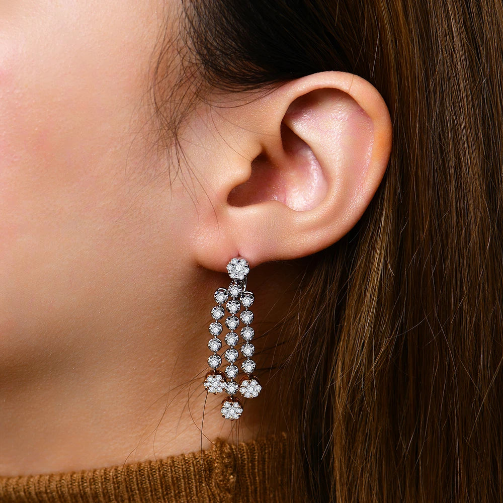 Close-up of an ear wearing a dangling earring with a neutral background