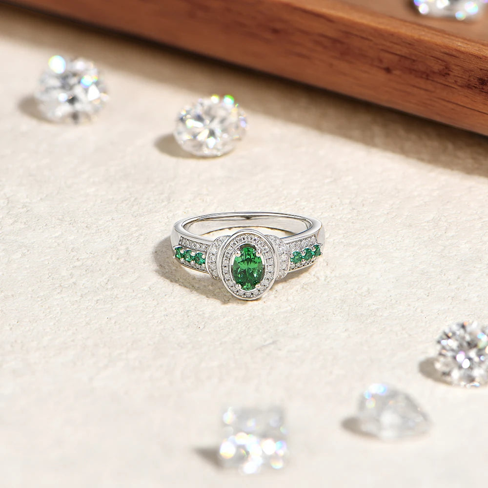 Silver ring with green gemstones on a beige surface with scattered diamonds.