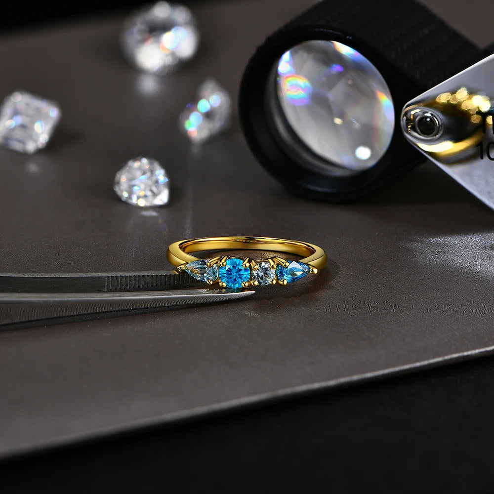 Gold ring with blue gemstones on a dark surface with diamonds and a magnifying glass.