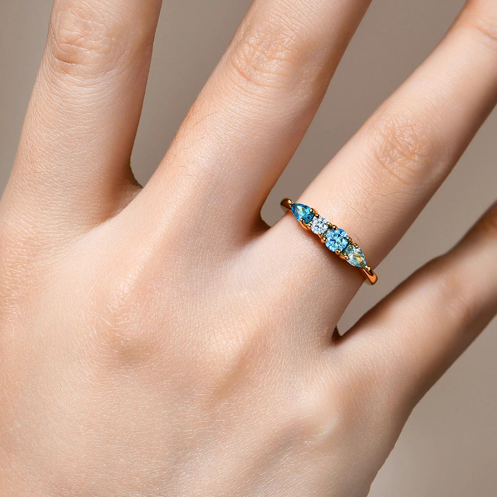 Gold ring with blue gemstones on a hand against a neutral background