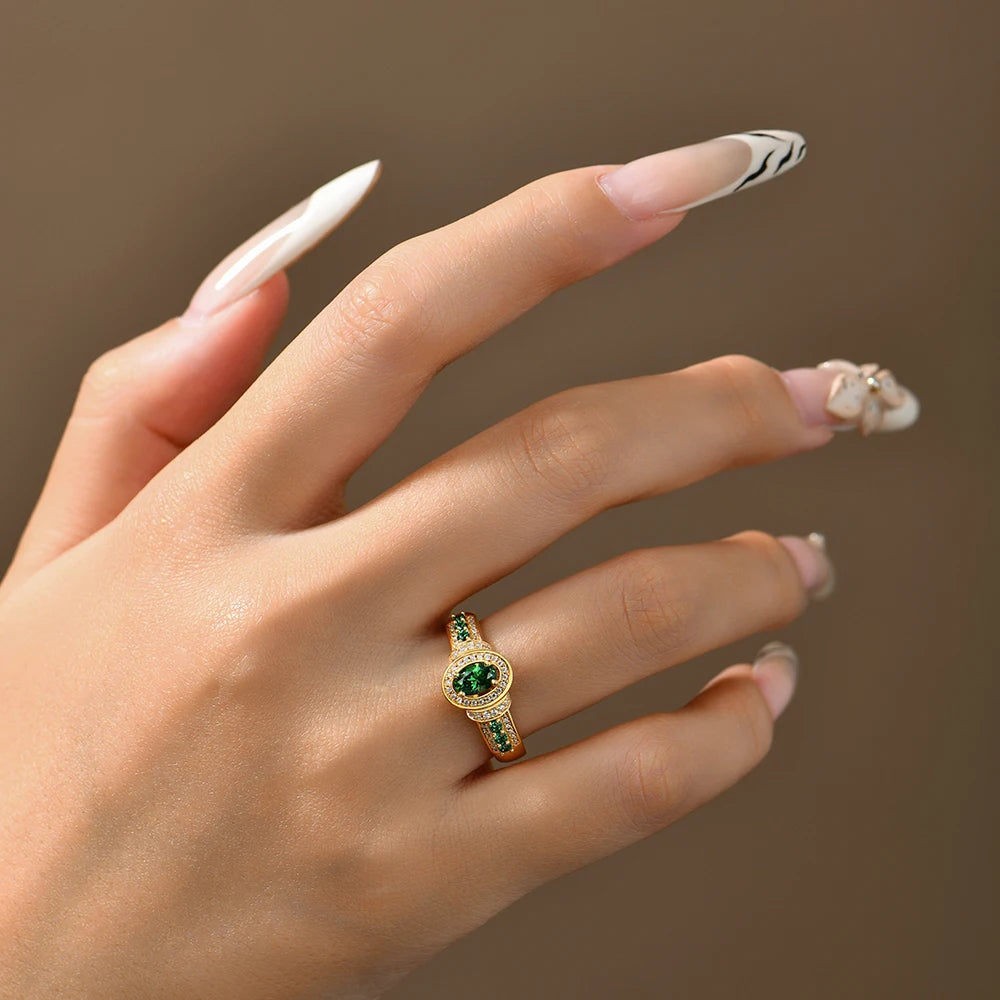 Hand wearing a gold ring with green gemstone against a neutral background