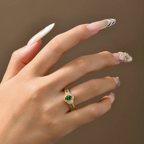 Hand wearing a gold ring with green gemstone against a neutral background